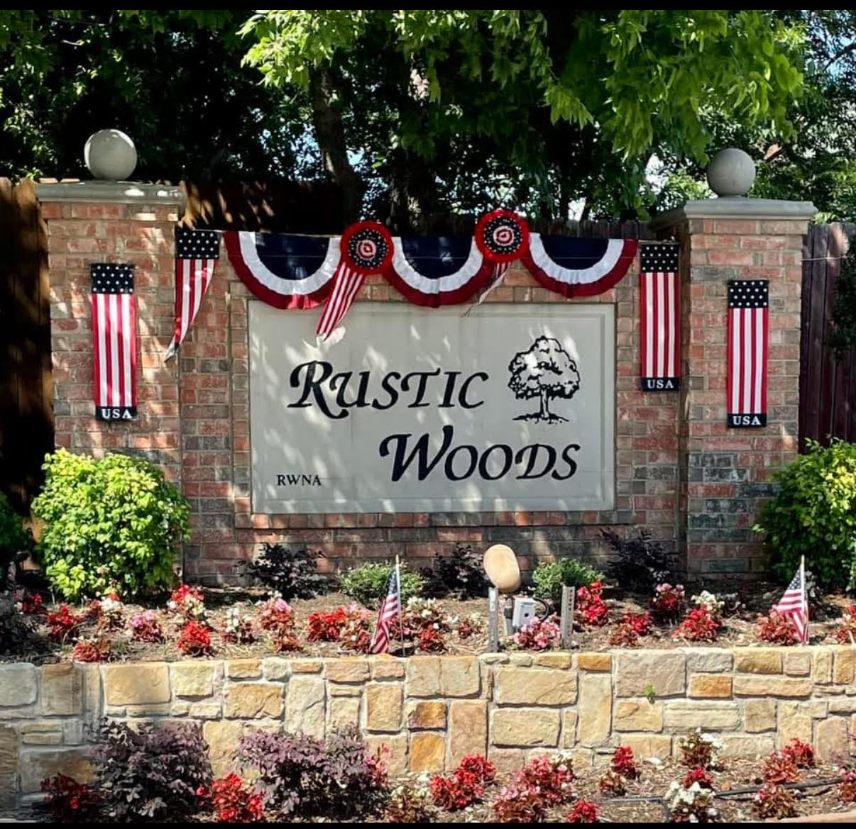 The brick Rustic Woods entrance monument with flowers and American flags